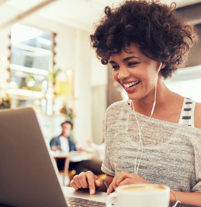 Image of happy woman using laptop while sitting at cafe. Young african american woman sitting in a coffee shop and working on laptop.