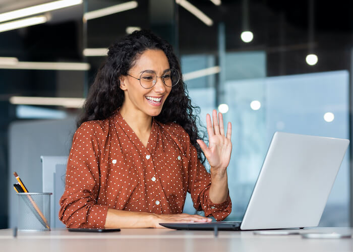 Successful and beautiful hispanic woman working inside modern office building, businesswoman using laptop for video call smiling and waving, greeting gesture, online conference with colleagues.