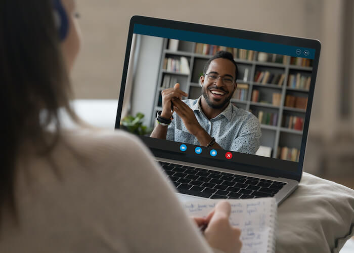Student girl in headphones making video call to happy African coach, teacher, tutor, watching learning webinar, blogger online presentation on laptop, writing notes, studying on internet
