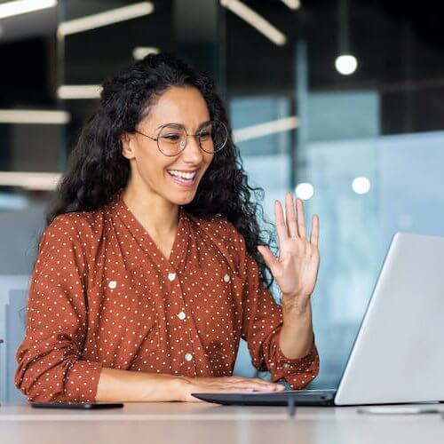 Successful and beautiful hispanic woman working inside modern office building, businesswoman using laptop for video call smiling and waving, greeting gesture, online conference with colleagues.
