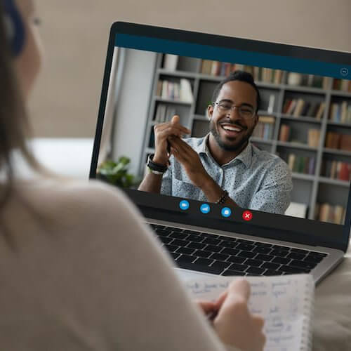Student girl in headphones making video call to happy African coach, teacher, tutor, watching learning webinar, blogger online presentation on laptop, writing notes, studying on internet